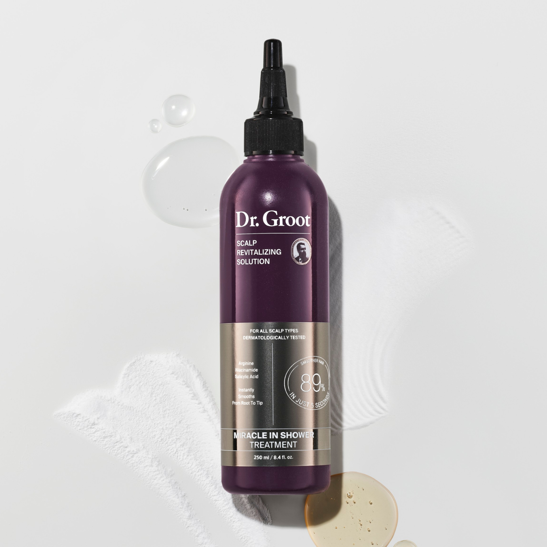 A dark purple bottle of Dr. Groot Miracle In Shower Treatment lying on a grey surface in a few drops of the tonic and two spreads of white powder.