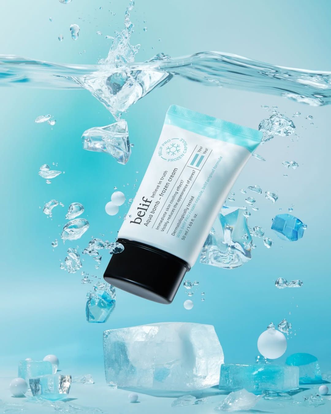 A tube of belif Aqua bomb – frozen cream floats in water with ice cubes and splashes against a light blue background.