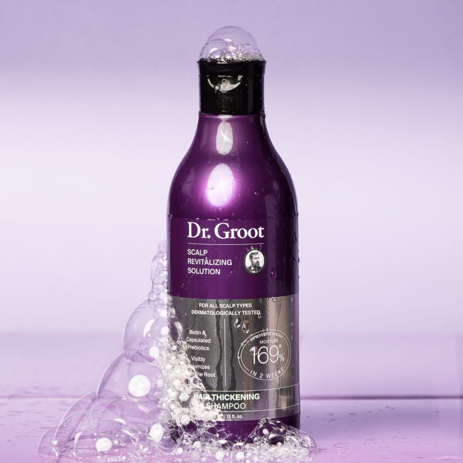 A purple Dr. Groot Hair Thickening Shampoo bottle with overflowing white bubbles against a lavender background.