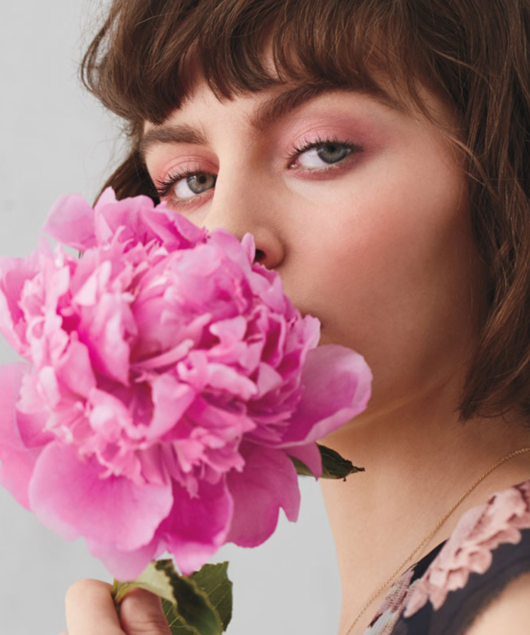A model holds a pink peony flower to her face.