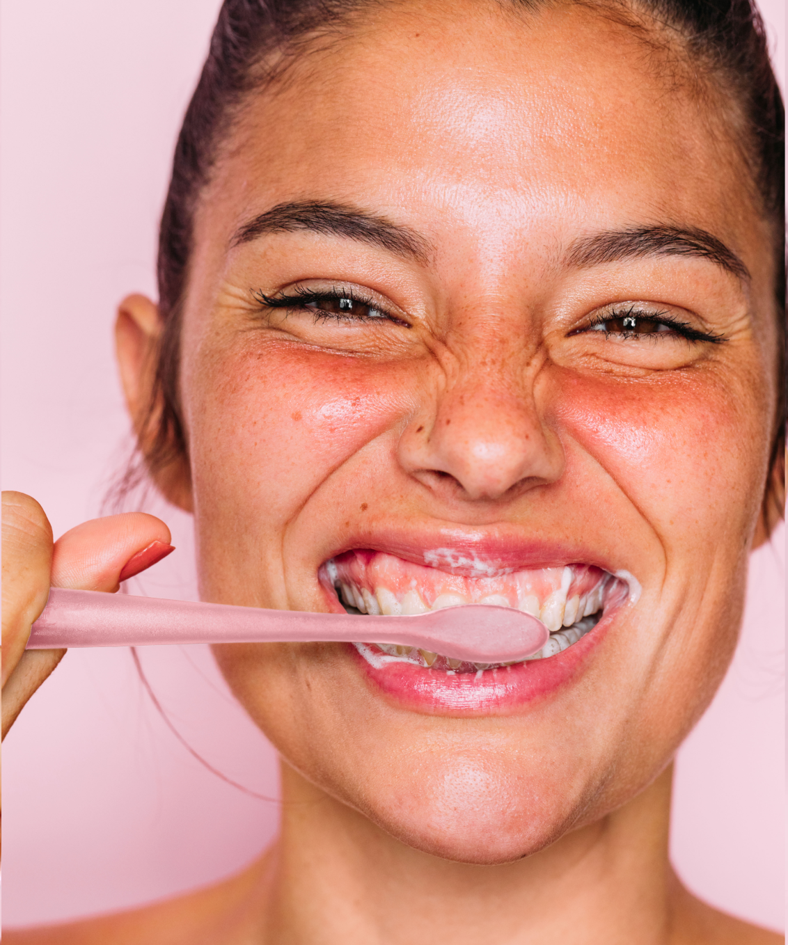 A widely smiling model brushing her teeth with a pink Euthymol Whitenin Toothbrush, looking right at the viewer
