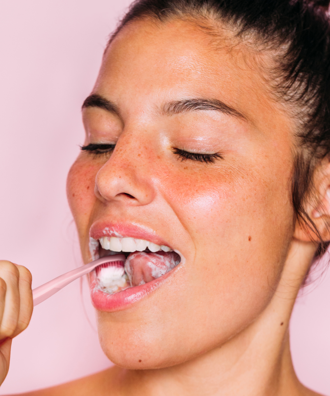 A slightly smiling model with her eyes closed brushing her teeth with a pink Euthymol Whitening Toothbrush