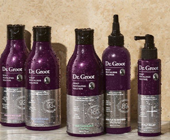 A range of Dr. Groot scalp care and shampoo products sit on a bathroom shelf alongside a Premium Cleansing Brush with ''$325 value'' seal in top left corner.