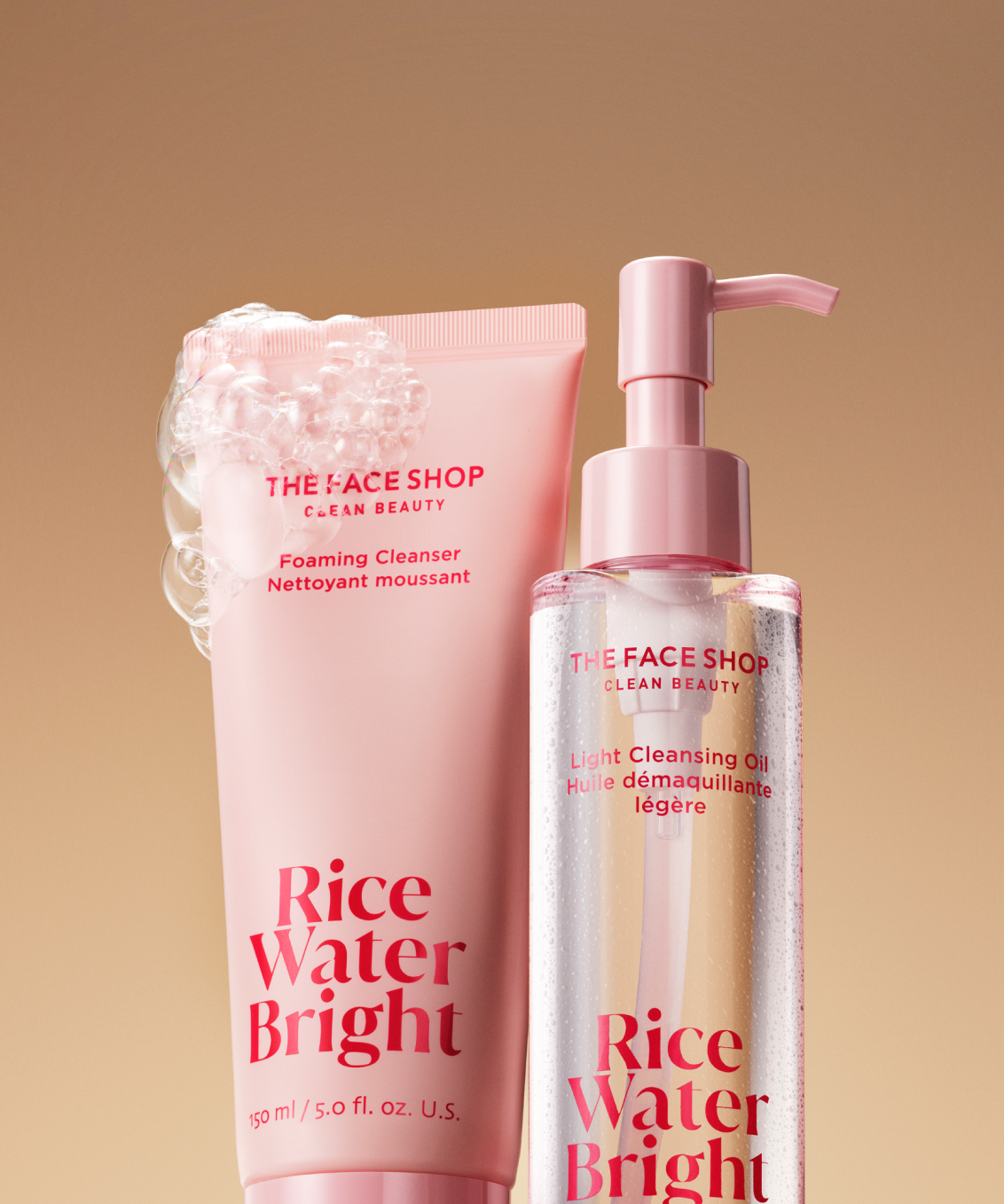 A bottle of The Face Shop Rice Water Bright Foaming Cleanser covered in bubbles next to a bottle of Light Cleansing Oil on a warm beige background.