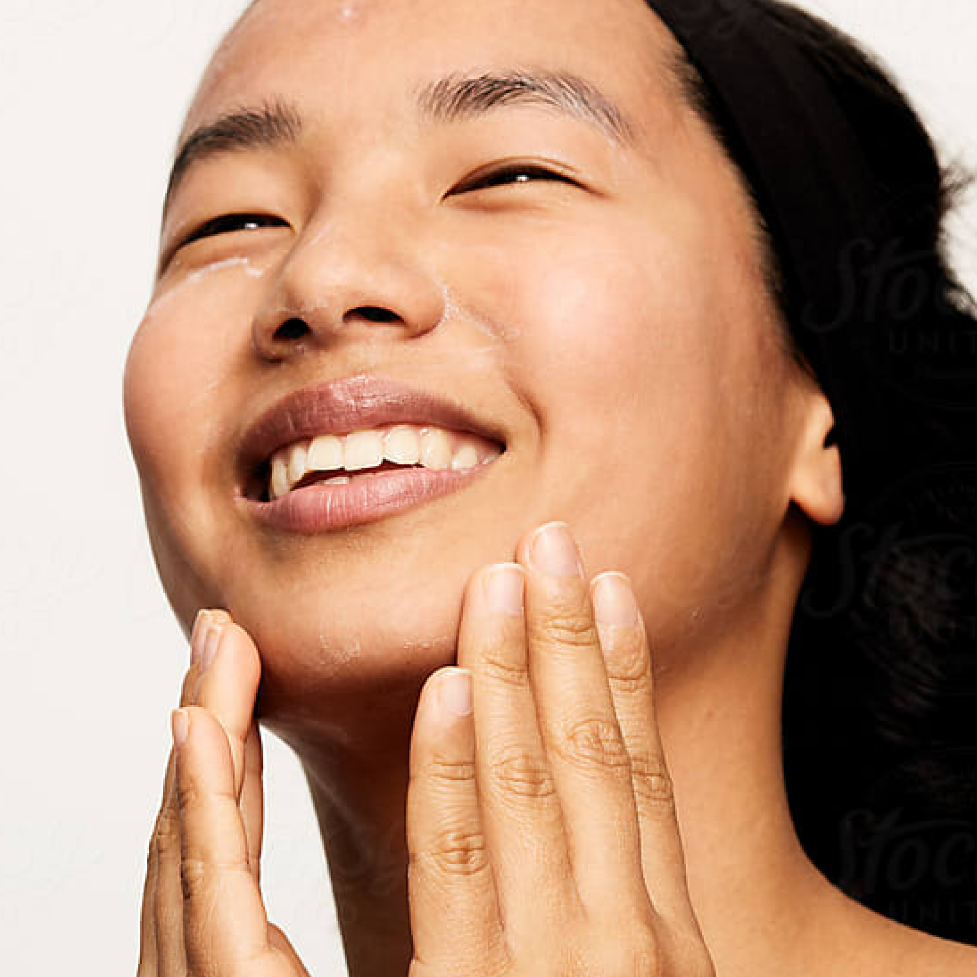 A model looking up and smiling, applying Physiogel Daily Moisture Lotion to her cheeks