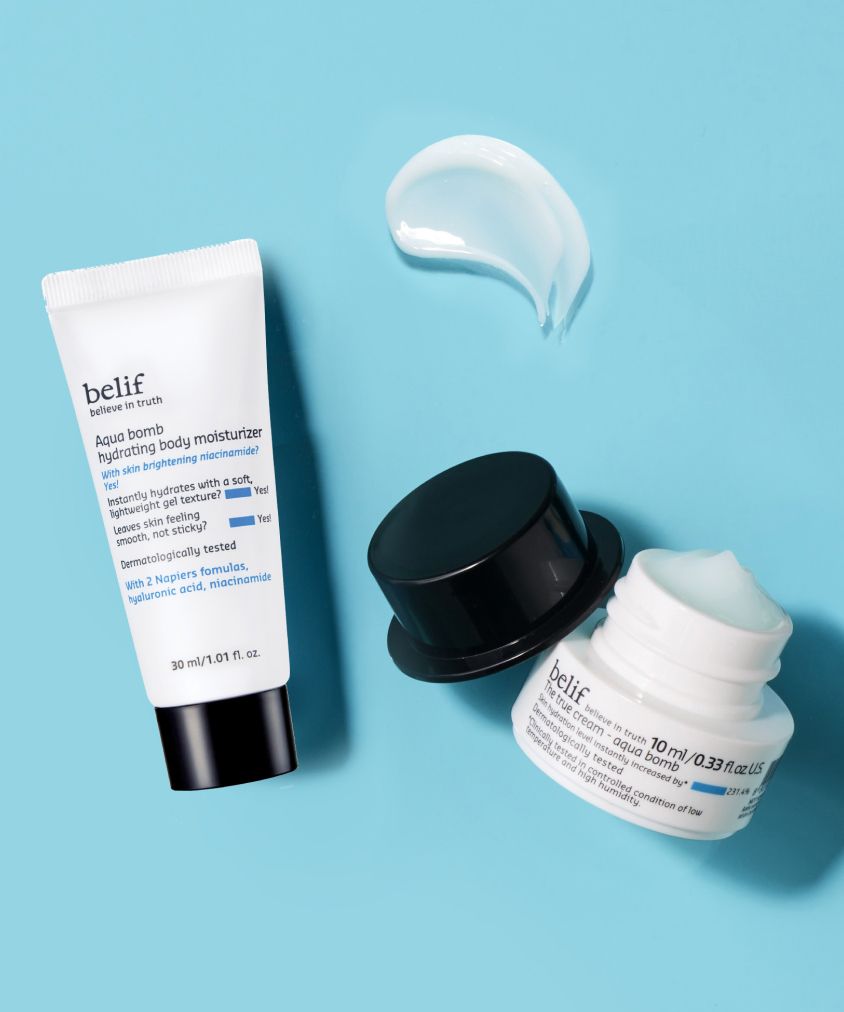 Two skin care products by belif on a light blue background: an open jar of Aqua Bomb True Cream showing its white contents and a tube of Aqua Bomb body moisturizer with a dab of cream beside it.