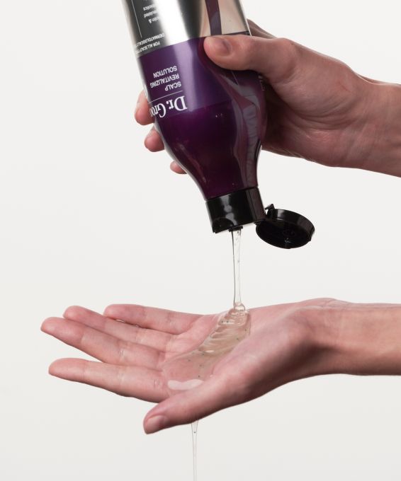A hand pours clear, textured Dr. G Scalp Revitalizing Solution from a purple bottle into an open palm.