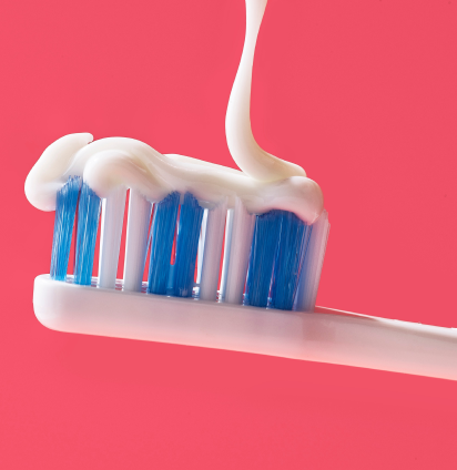 A white-and-blue toothbrush with a POP Kids Gel Pumpin' Strawberry Toothpaste pouring on it from above on the pink background.