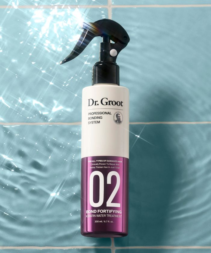 A white and purple bottle of Dr. Groot Professional Bonding System Bond Fortifying #2 Keratin Water with black sprinkler lying on a light blue tile floor