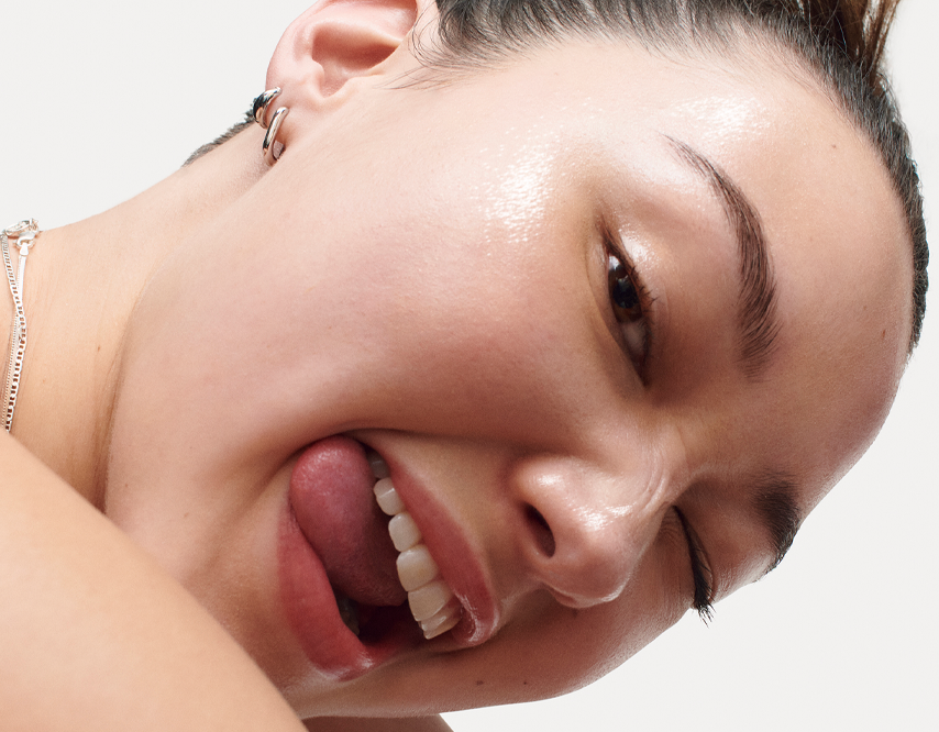A close up of a young model smiling and playfully biting her tongue.