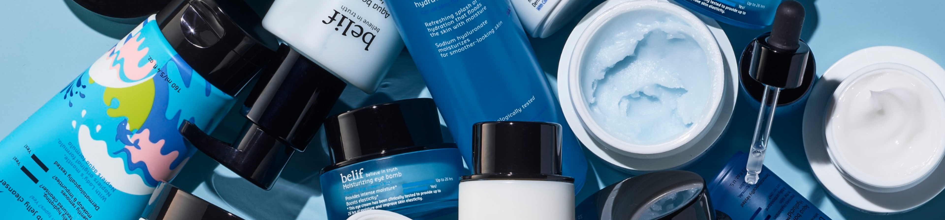 A collection of belif skincare products is scattered across a light blue background with some containers open and others closed