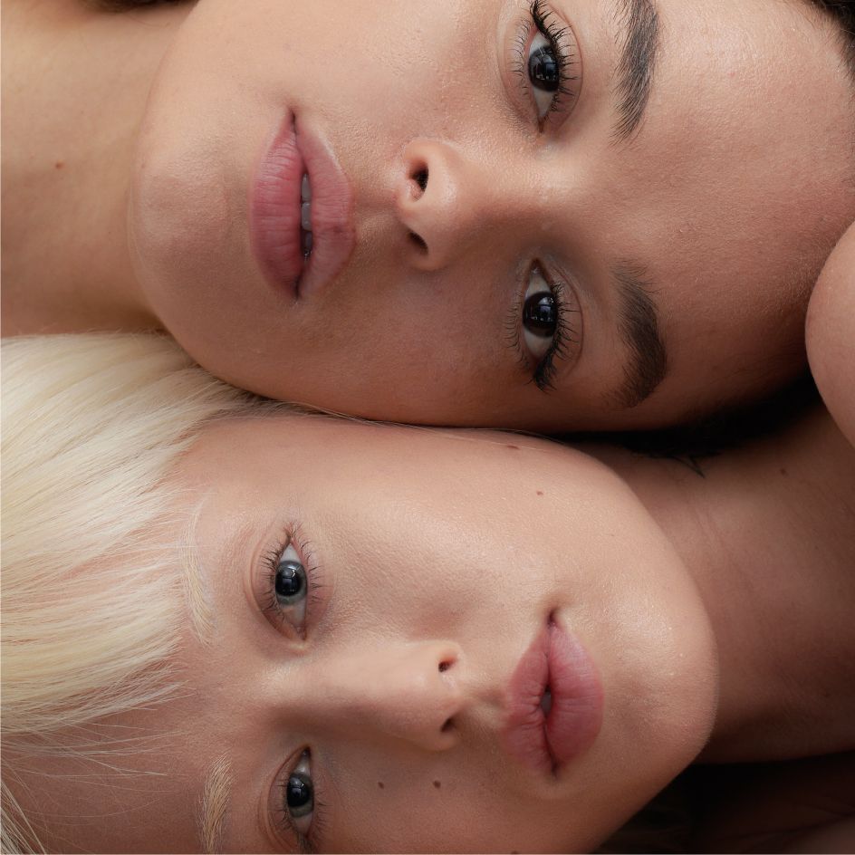 Close-up of two people lying down with their heads touching, showcasing their faces and expressive eyes.