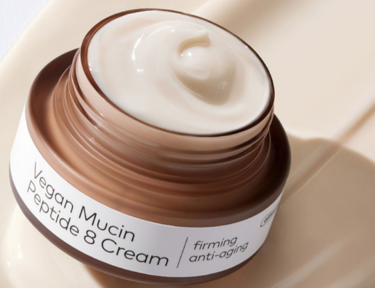 Open brown jar of white Vegan Mucin Peptide 8 Cream, labeled "firming anti-aging."