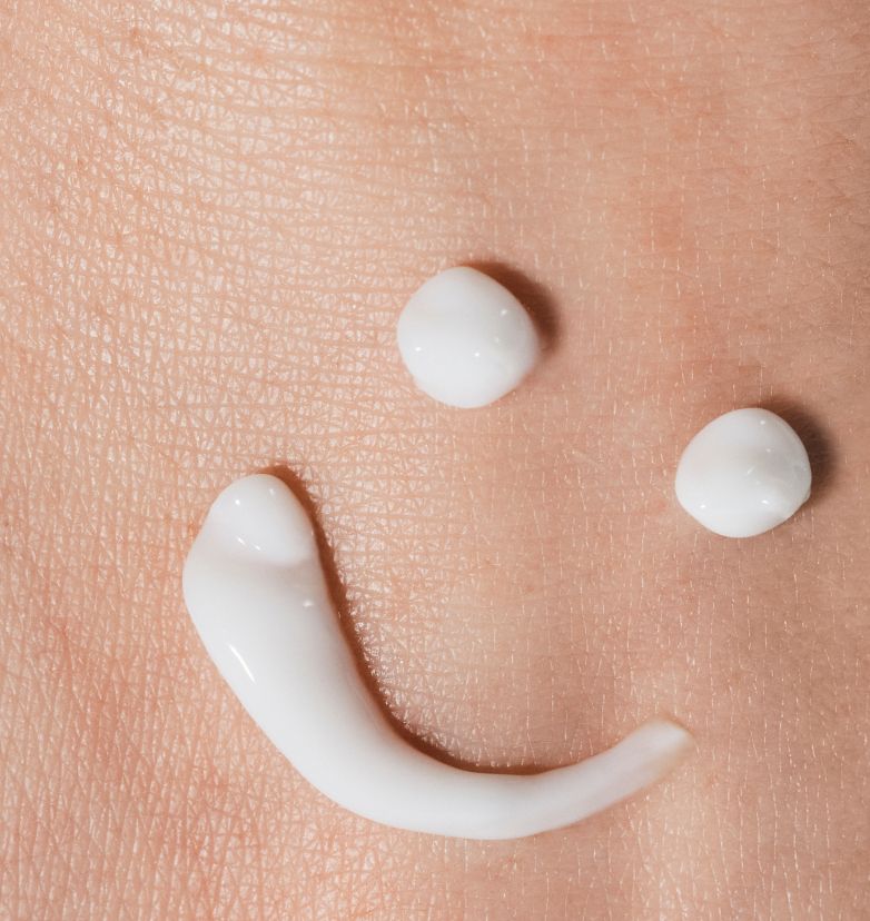 Smiley face drawn on a hand with cream moisturizer, symbolizing happiness and positivity.
