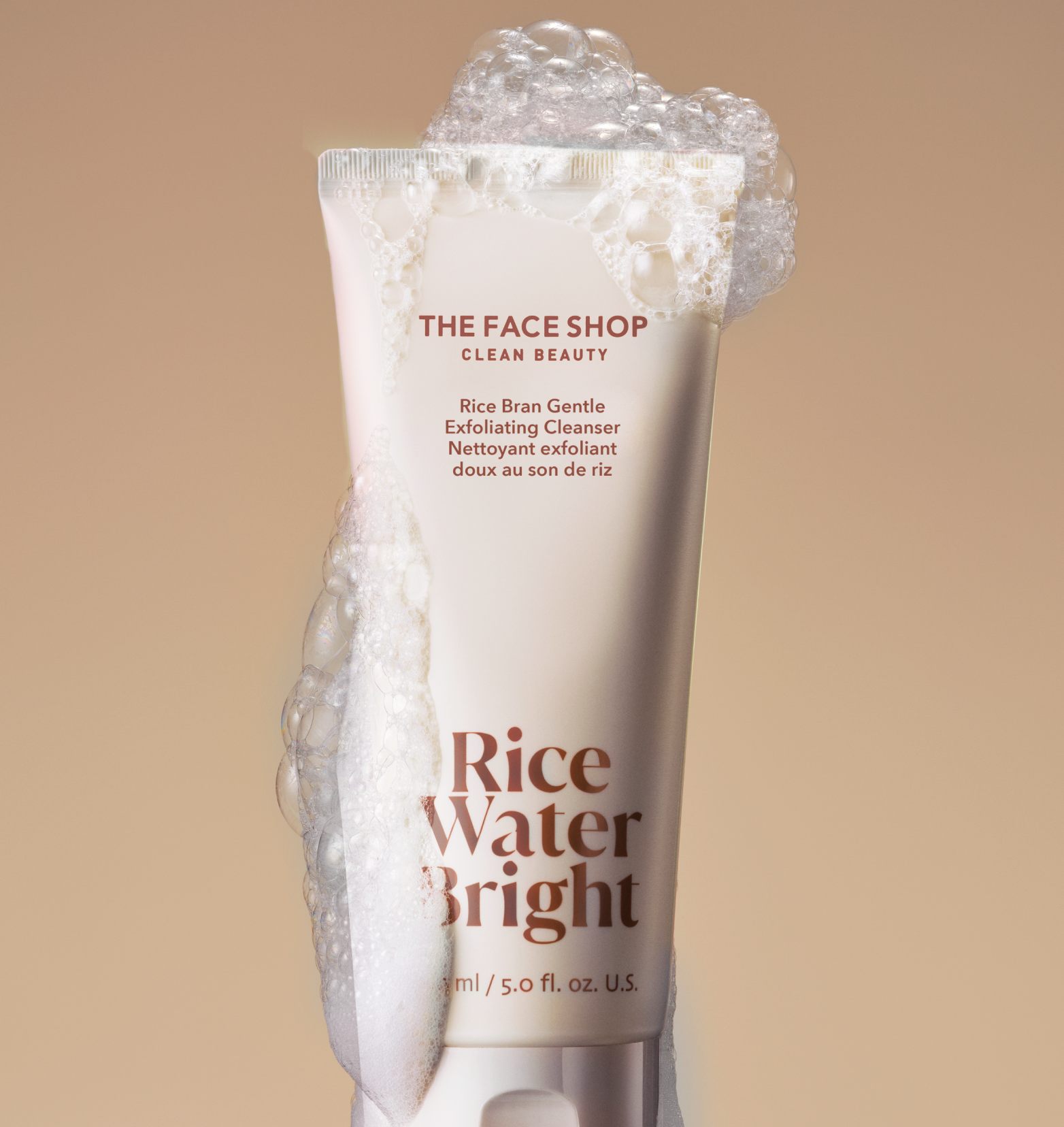 A tube of Rice Water Bright Rice Bran Gentle Exfoliating Cleanser covered in bubbles on a beige background.