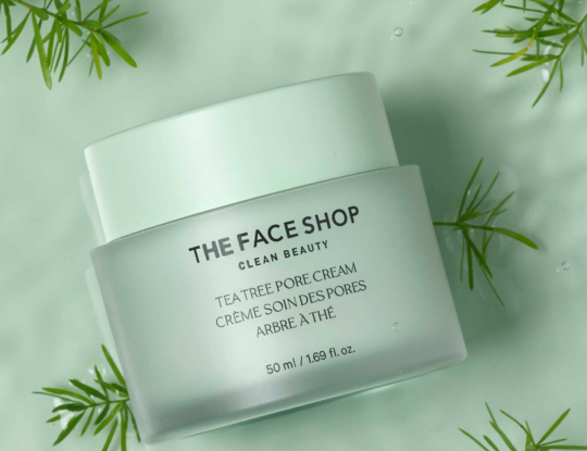 Frosted jar of The Face Shop Tea Tree Pore Cream on a light green surface with water and green leaves.