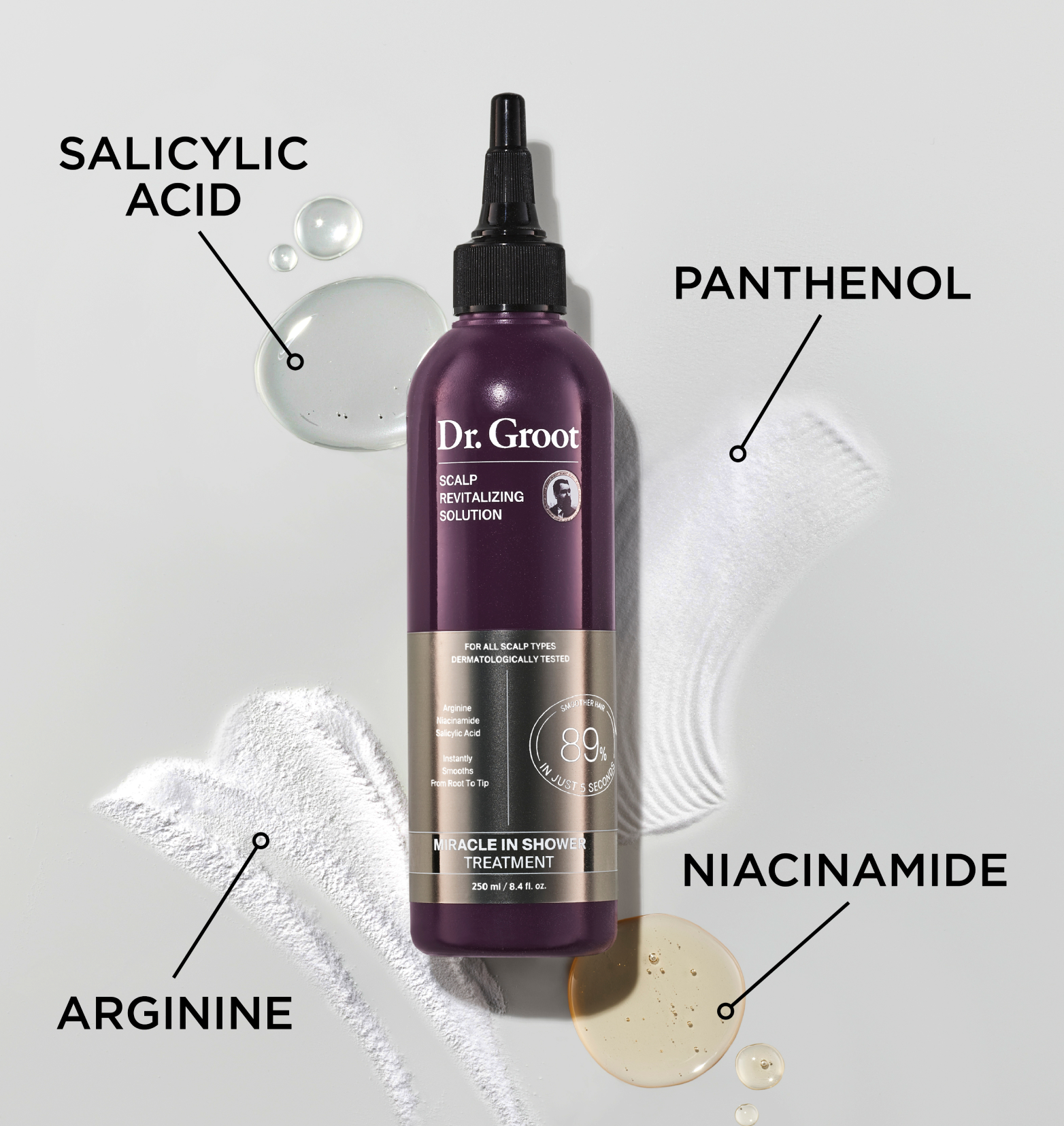 A dark purple bottle of Dr. Groot Miracle In Shower Treatment rests on a spread of panthenol, drop of salicylic acid, a drop of niacinamide, and a spread of arginine..
