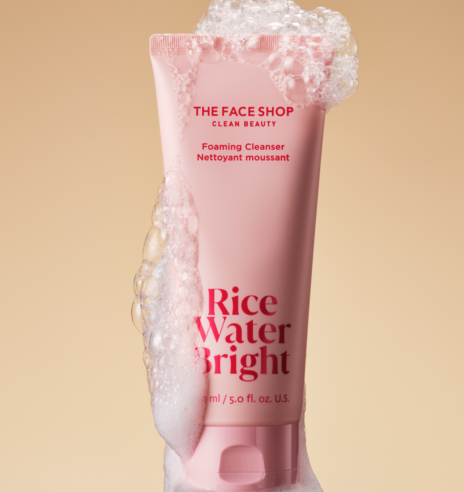 A tube of the face shop rice water bright cleansing foam covered in bubbles is displayed on a warm beige background.
