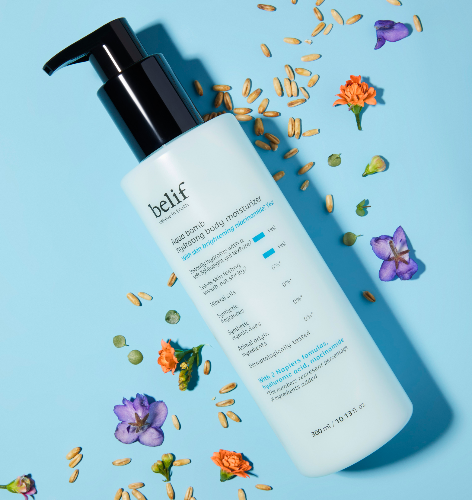 A white bottle of belif Aqua Bomb Hydrating Body Moisturizer lying on a light blue surface with a bunch of seeds and flowers scattered around