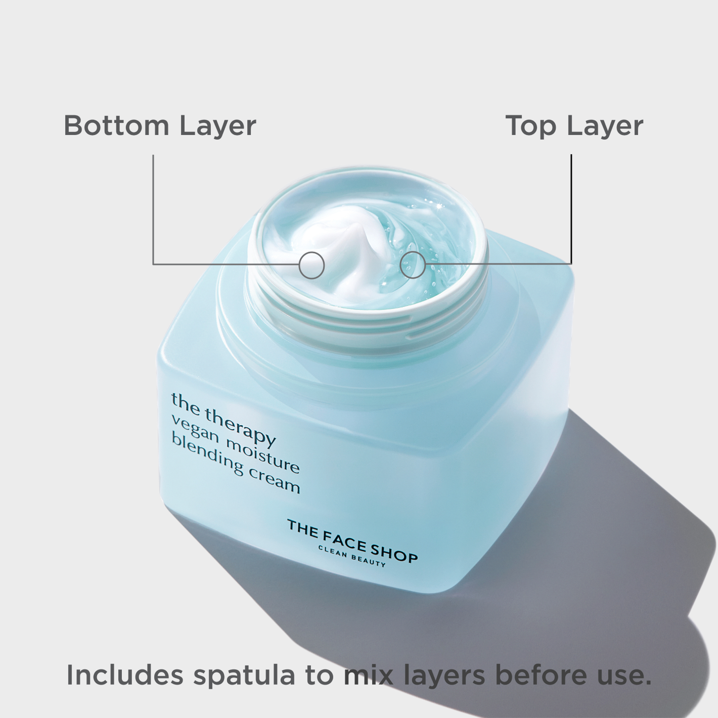 A light blue jar of The Face Shop Vegan Moisture Blending Cream with the lid opened showing the cream texture and three indicators pointing at the Bottom layer texture, and at the Top layer texture, as well as a disclaimer that says "Includes spatula to mix layers before use".