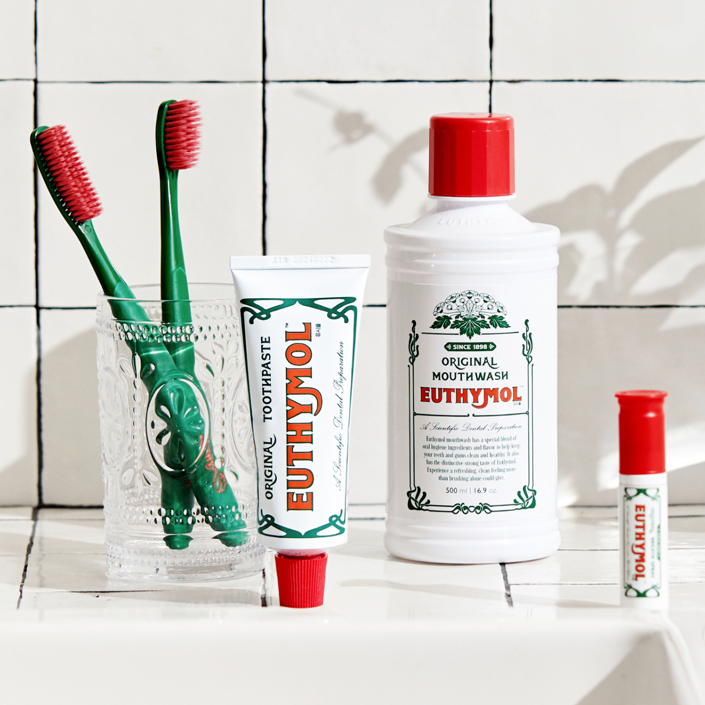 Euthymol Original Toothbrushes,, a tube of toothpaste, and a bottle of mouthwash arranged on a tiled bathroom counter.