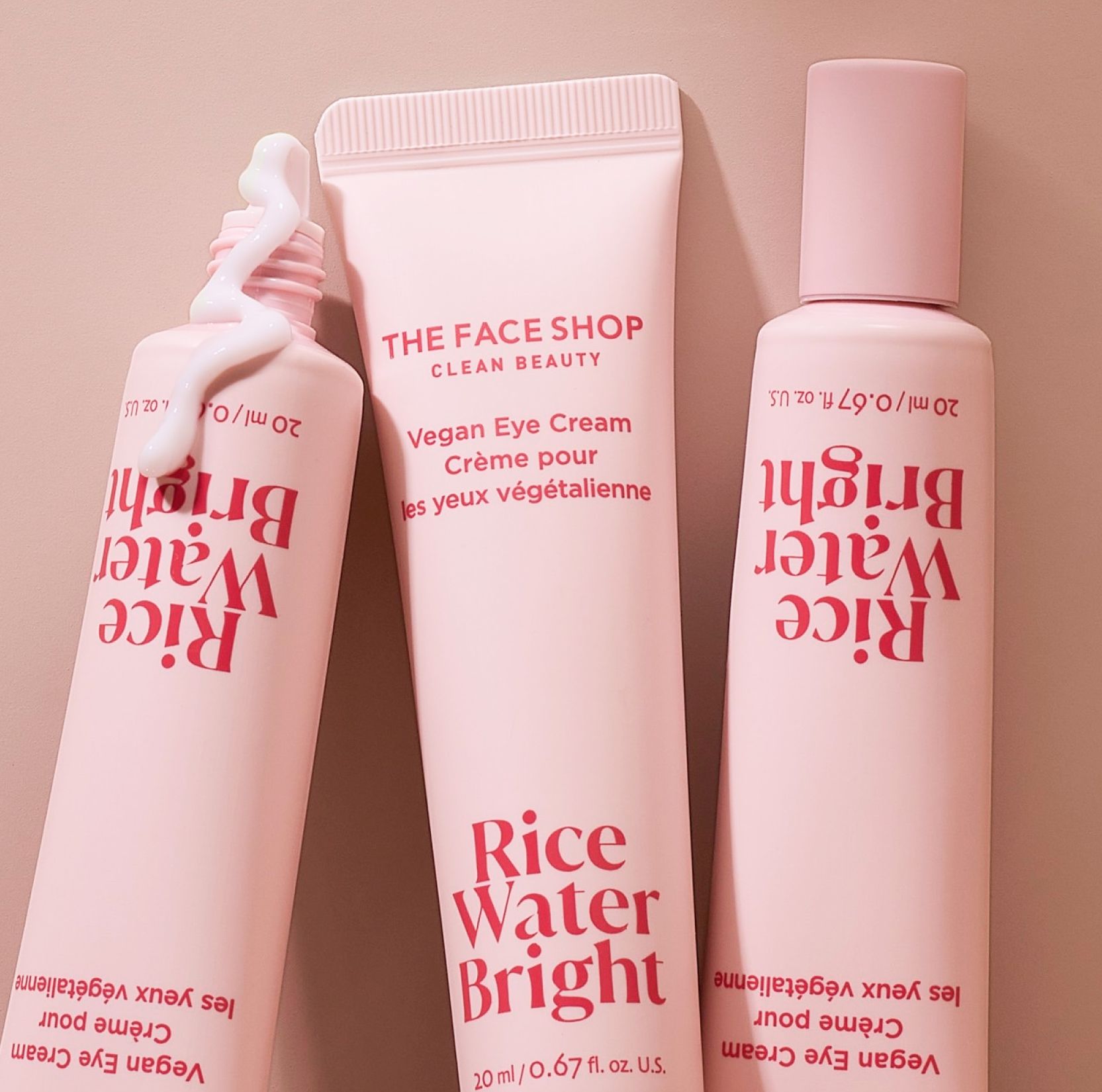 Three pink tubes of The Face Shop Rice Water Bright Vegan Eye Cream, two standing upside down with one with cream squeezed out.