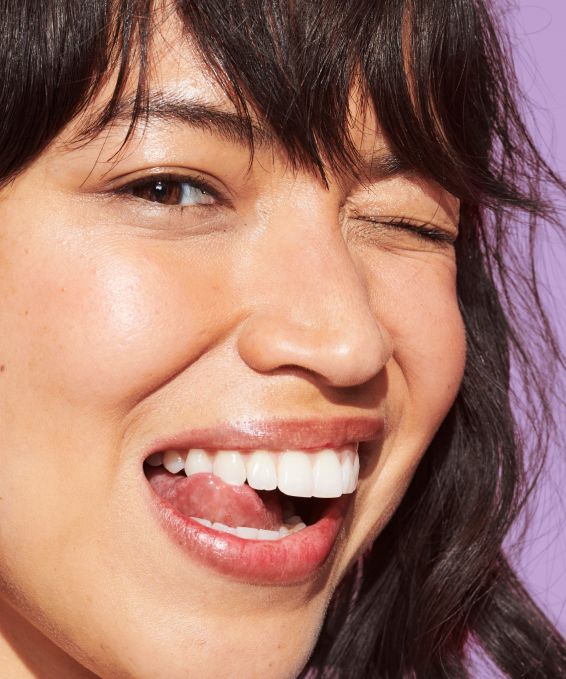 A model smiling and winking at the viewer, showing her teeth perfectly white and clean and shiny after using Reach POP Whitening Peppermint Twist Dental Floss