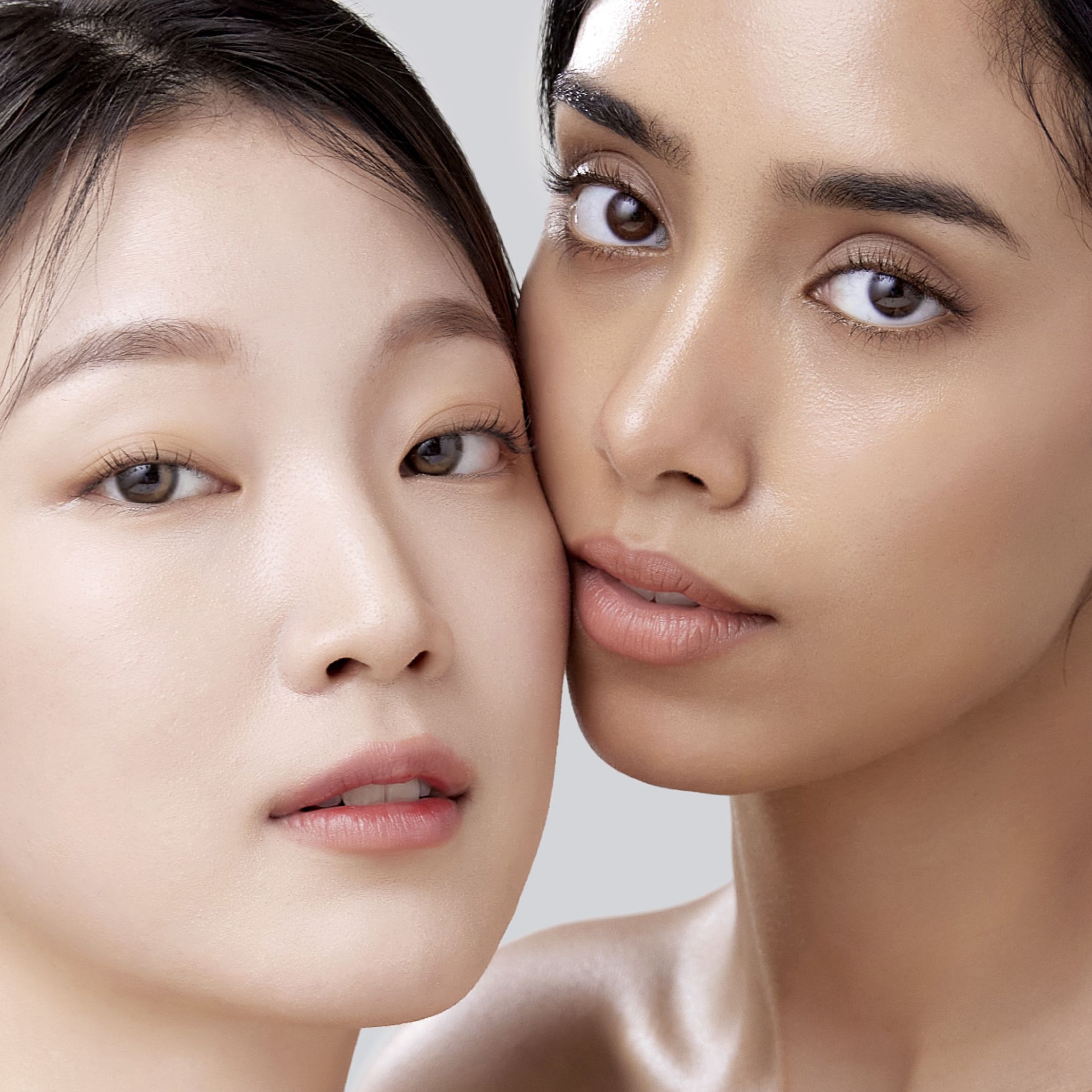 Two women with different skin tones posing for a photo, their cheeks touching, showcasing diversity and friendship.