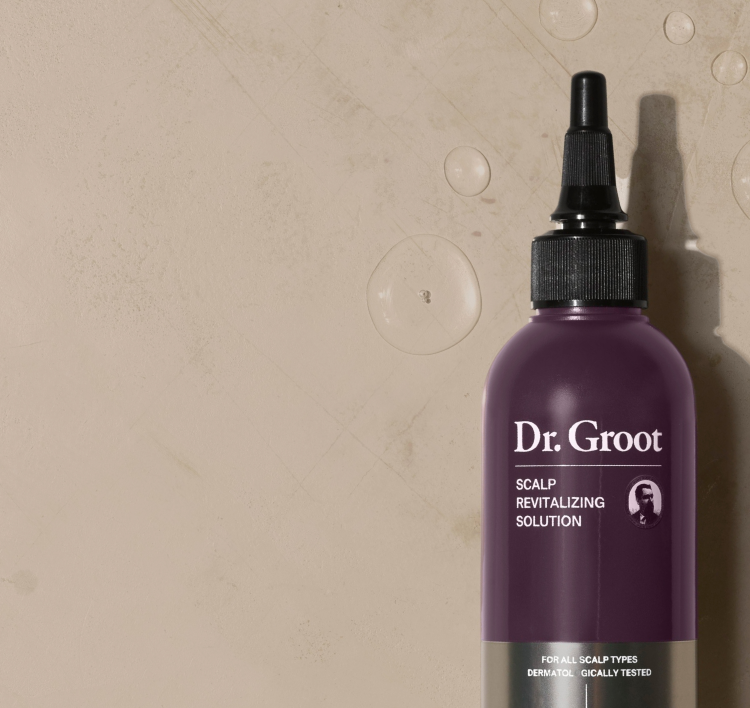 A dark-purple bottle of Dr. Groot Scalp Revitalizing Solution Miracle In Shower Treatment lying on a beige surface with a few drops around it.