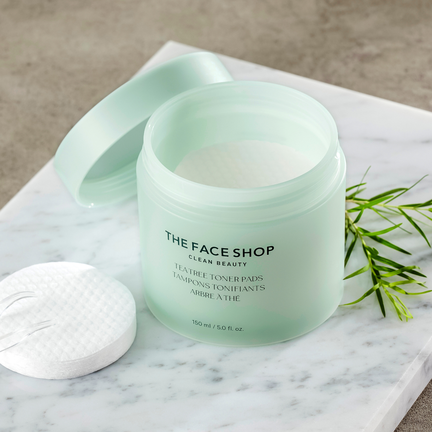 A opened light green jar of The Face Shop Tea Tree Toner Pads standing on a marble surface