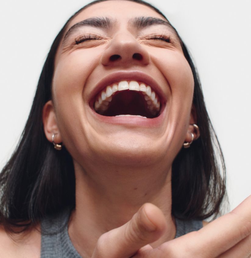 A closeup of a woman laughing with her eyes closed and head titled back.