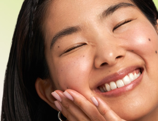Close-up of a person with closed eyes smiling broadly and touching their cheek.