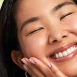 Close-up of a person with closed eyes smiling broadly and touching their cheek.