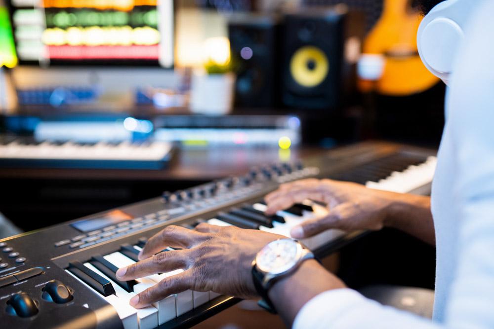 Hands of young African-american musician over keys of pianoboard working alone in contemporary sound recording studio