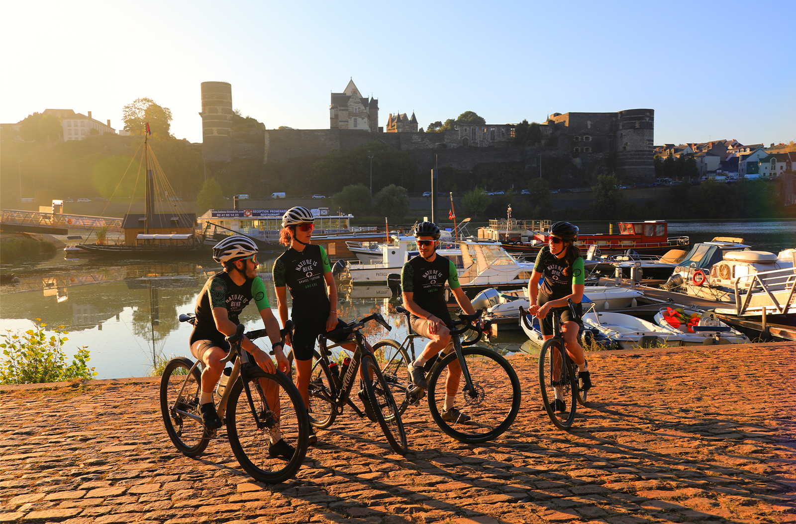 Gravel riders at golden hour along the Maine river with Angers castle behind them