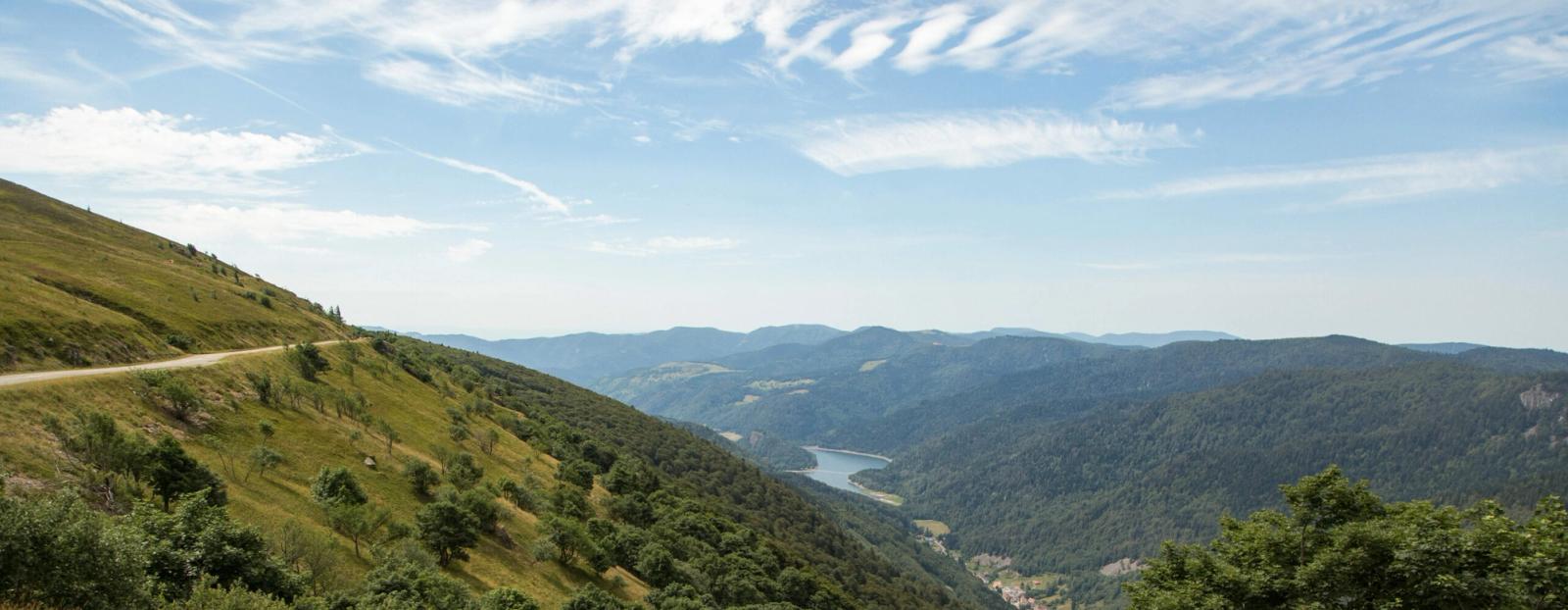 Sweeping gravel road along a Vosges mountain ridge overlooking a forested valley and lake