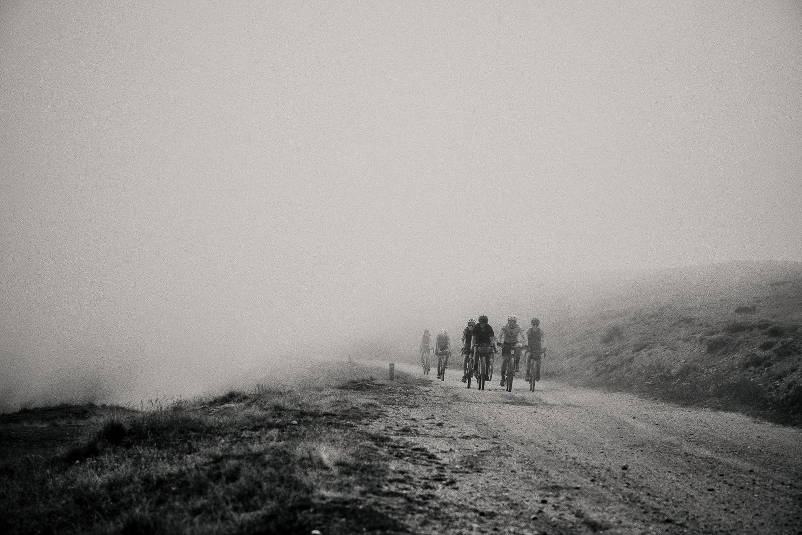 Riders climbing through dust and fog on a gravel mountain pass, Le Pilgrimage