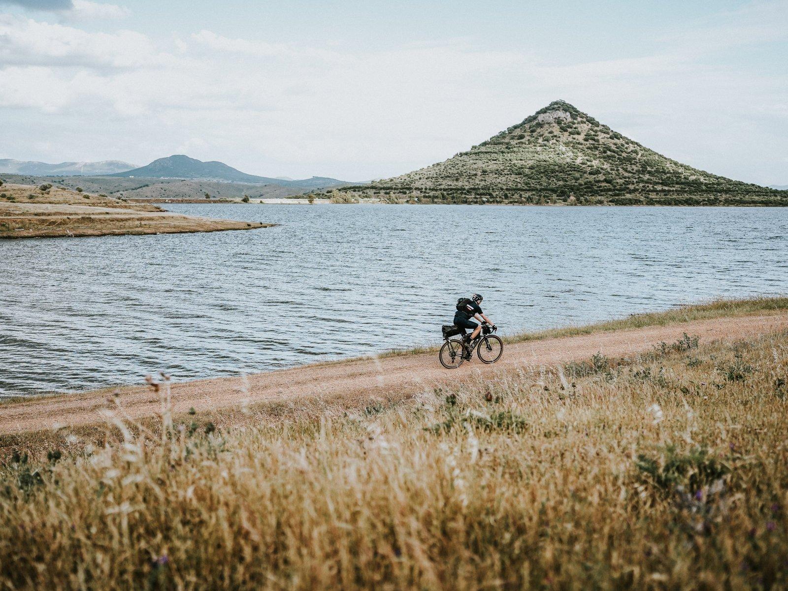 Bikepacker on a gravel track along a reservoir below a conical hill