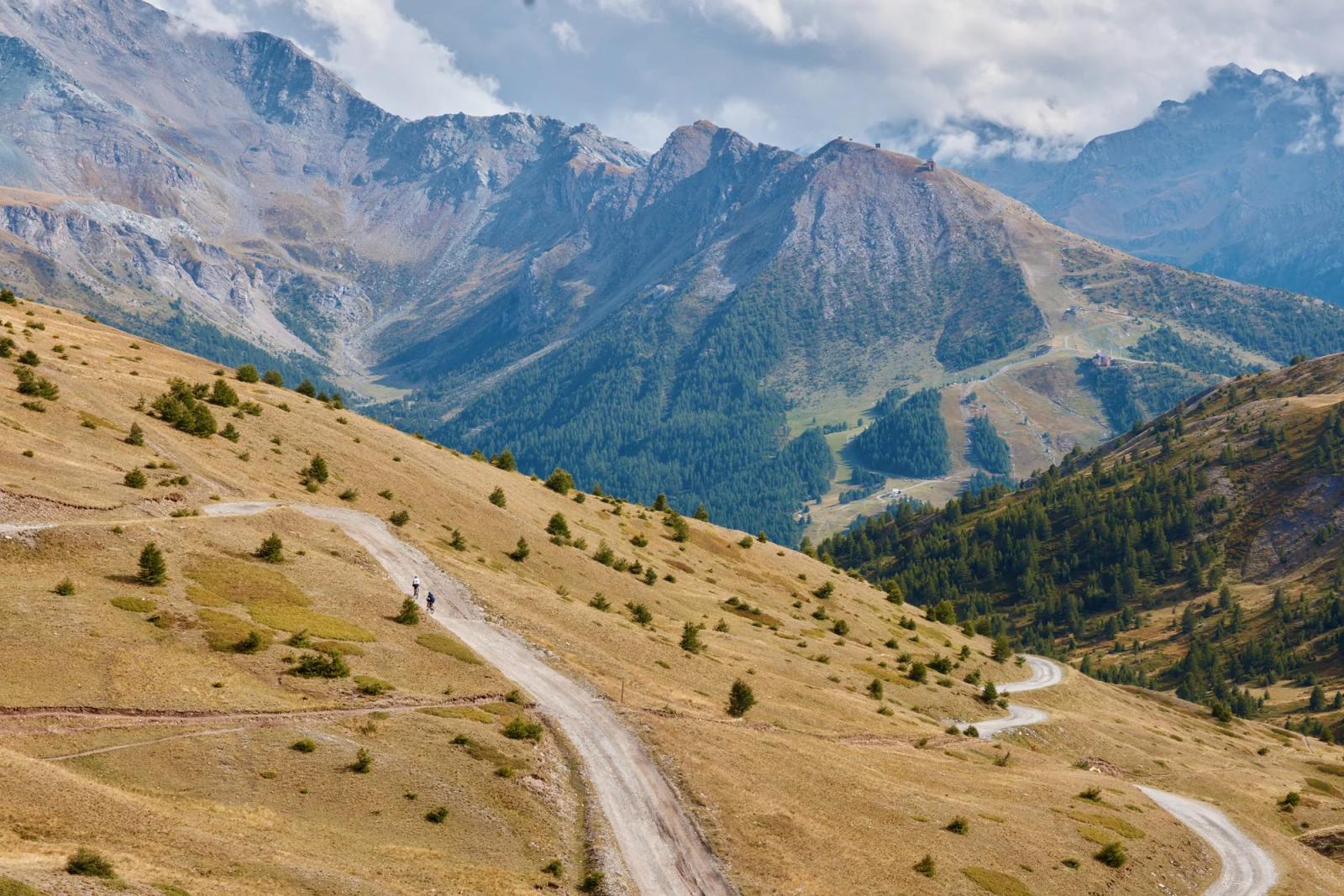 Riders on a winding gravel road through an alpine valley