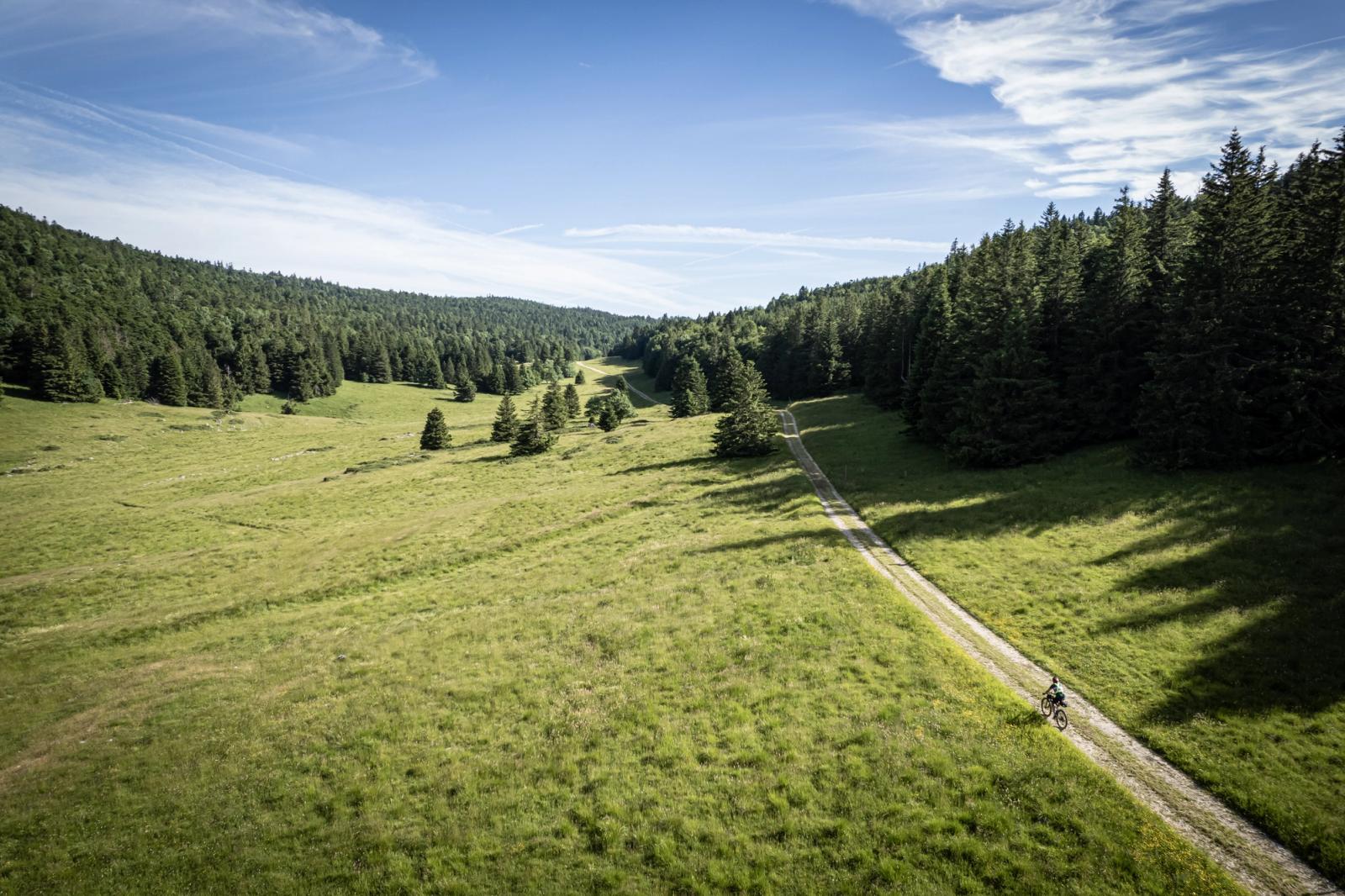 Aerial view of a gravel track through the Vercors valley, lone distant rider