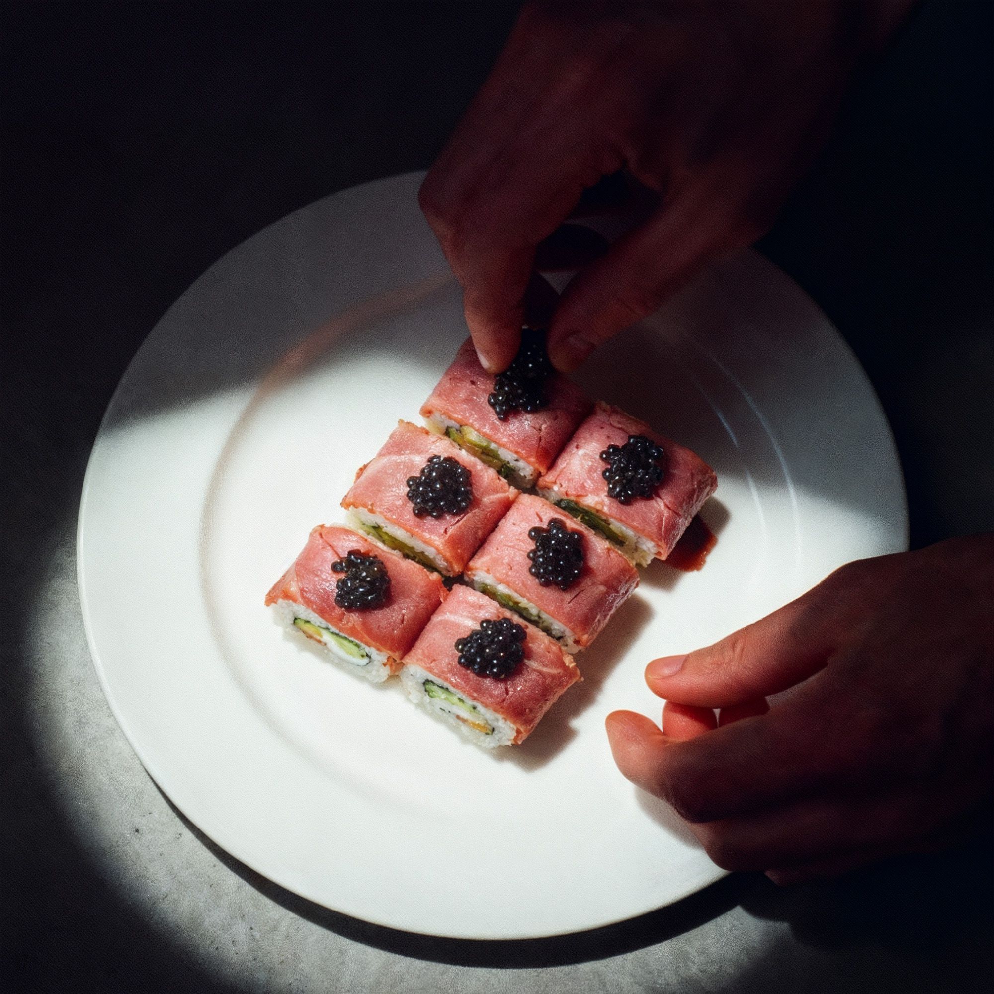 Sushi on a white plate with hands placing caviar on top on a concrete table