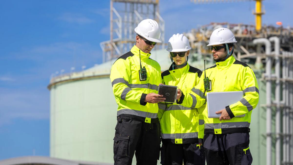 Two operators reviewing settings on a machine control panel during a shift handover.