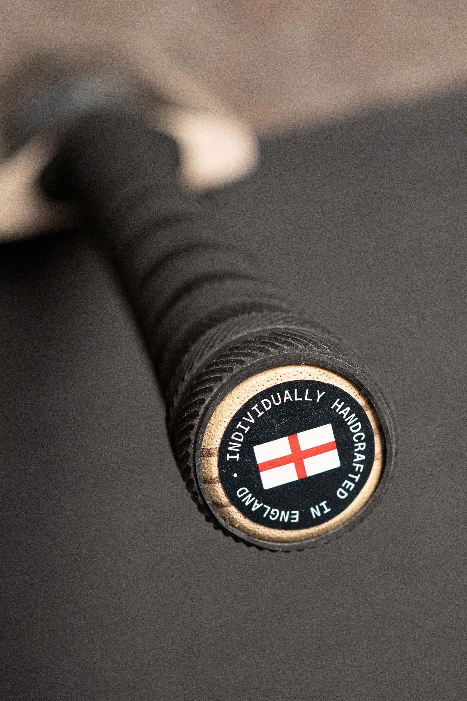 Close-up of a black cricket bat grip with a circular Made in England end label.