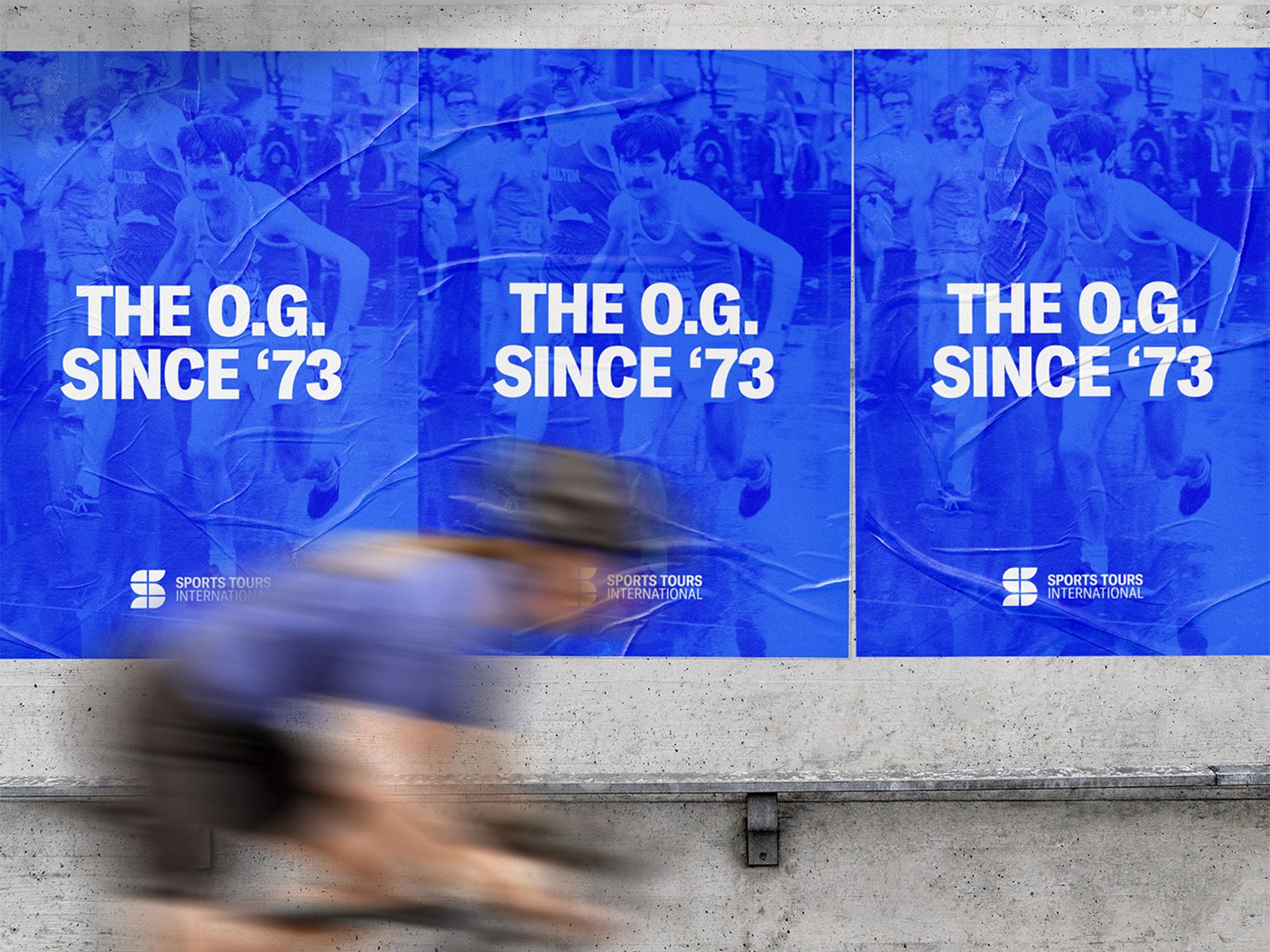 Blue Sports Tours International street posters reading The O.G. Since ’73, with a cyclist passing in front.