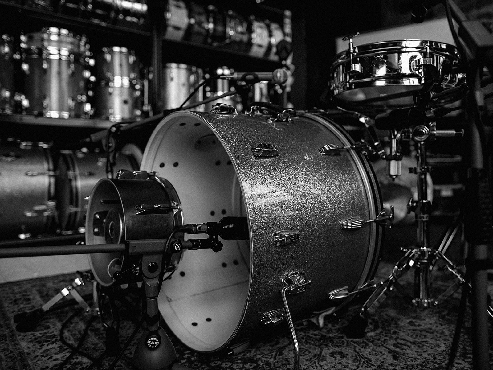 Black-and-white close-up of a drum kit surrounded by vintage recording equipment.