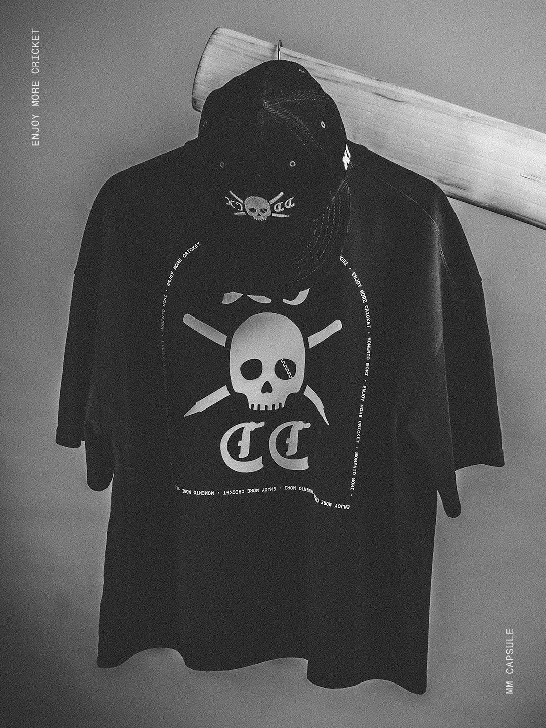 Black Eleven Cricket Club T-shirt with a white skull-and-crossed-bats graphic hanging against a grey wall.