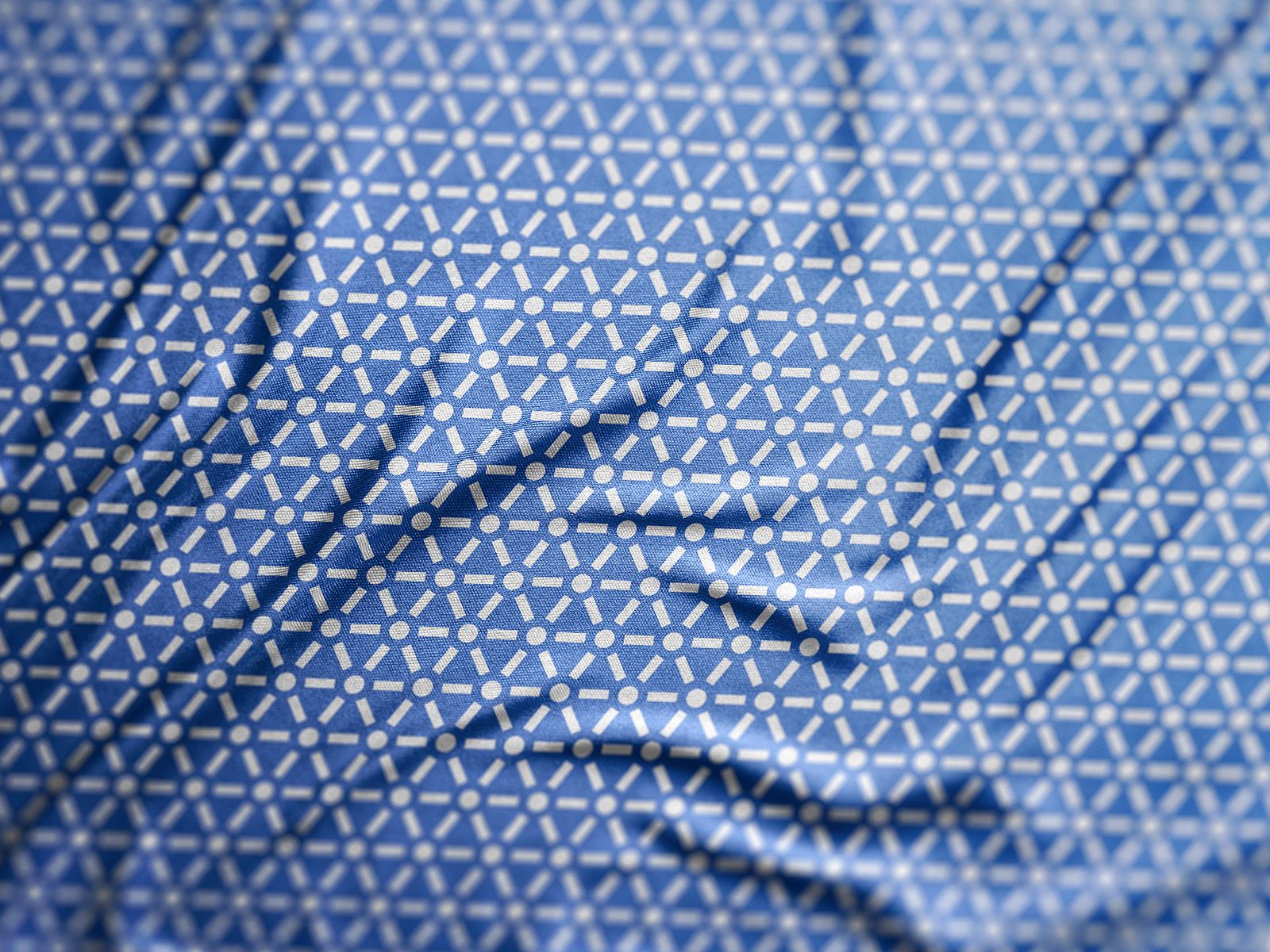 Close-up of blue fabric printed with a repeating light geometric Six Connections pattern.