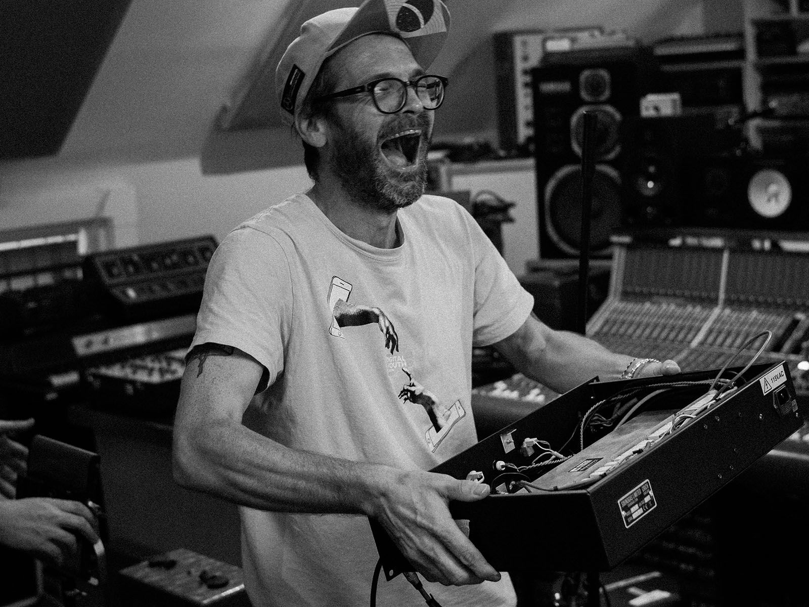 A person laughing while holding electronic music equipment in a recording studio.