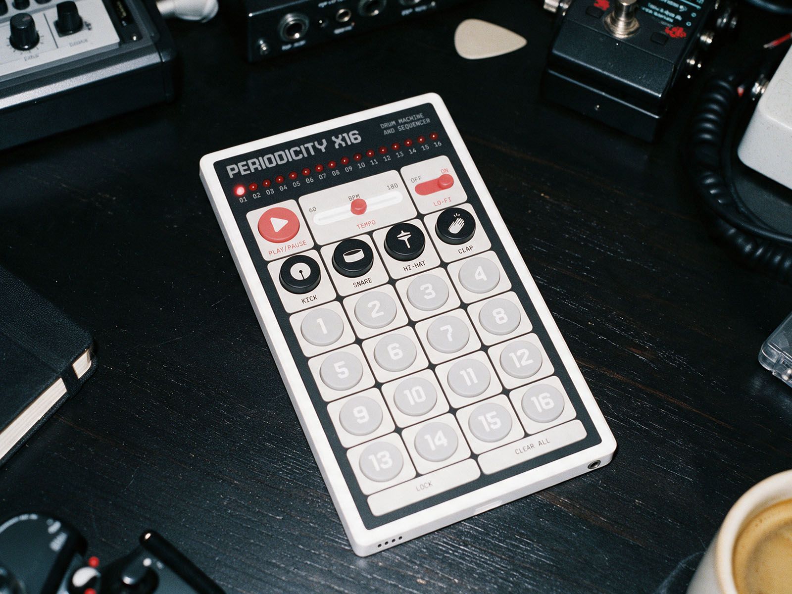 X16 hardware drum machine and sequencer on a black desktop surrounded by other musical equipment