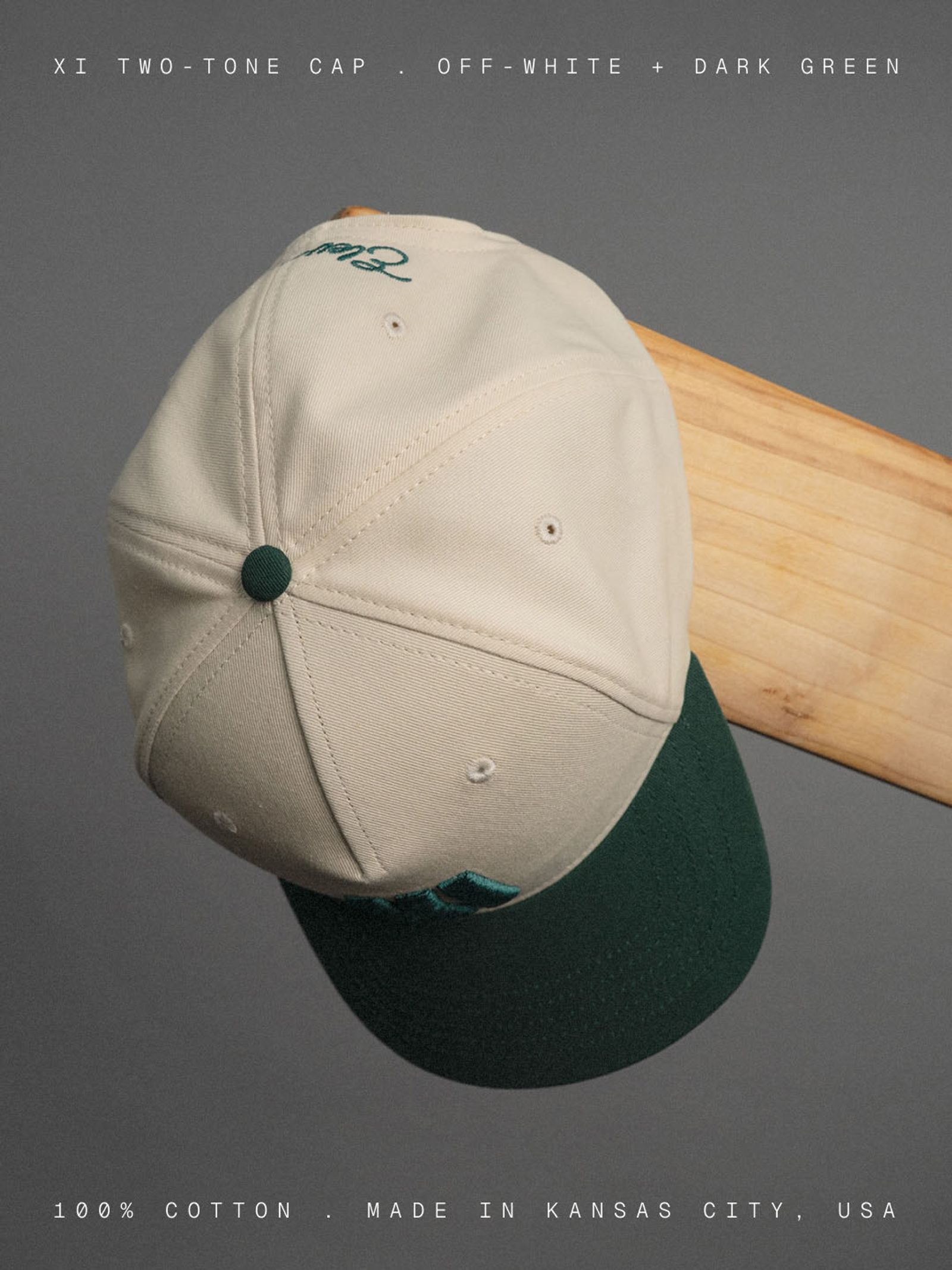 Cream-and-green Eleven Cricket Club cap hanging from a wooden bat against a grey background.